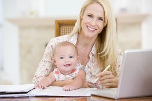 Mother and baby in dining room with laptop smiling